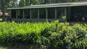 Ein Gebäude mit überdachter Terrasse, umgeben von üppiger Vegetation und hohen Bäumen.