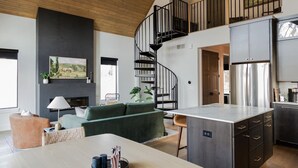 A modern kitchen with a large island, a spiral staircase, and a dining area with a sofa and table.