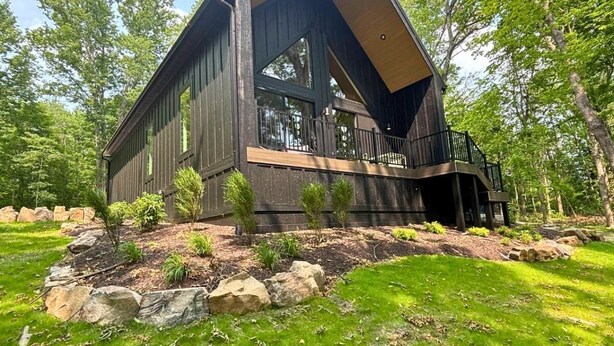 A modern two-story house with a balcony, surrounded by a landscaped garden with rocks and small trees.