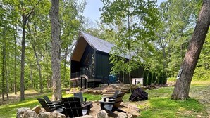 A cabin with a deck, surrounded by a natural setting with trees and outdoor seating.