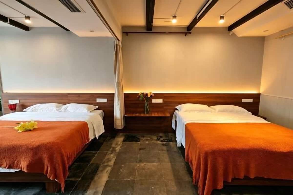 Habitación de hotel con dos camas, cabecero de madera, una mesita con un florero y suelo de baldosas.