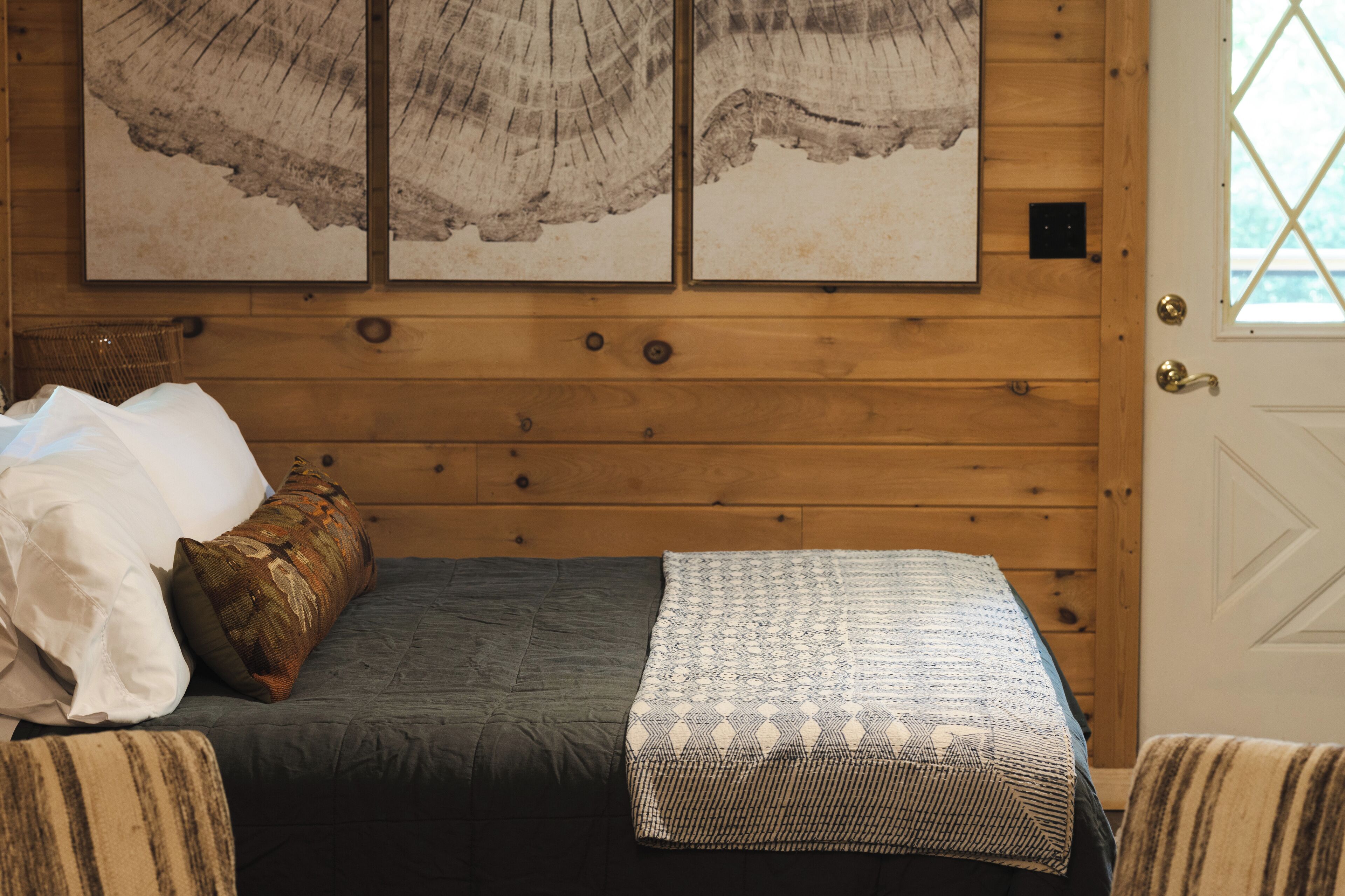 A wooden-paneled room with a bed, pillows, and a blanket. There are three framed pictures on the wall.