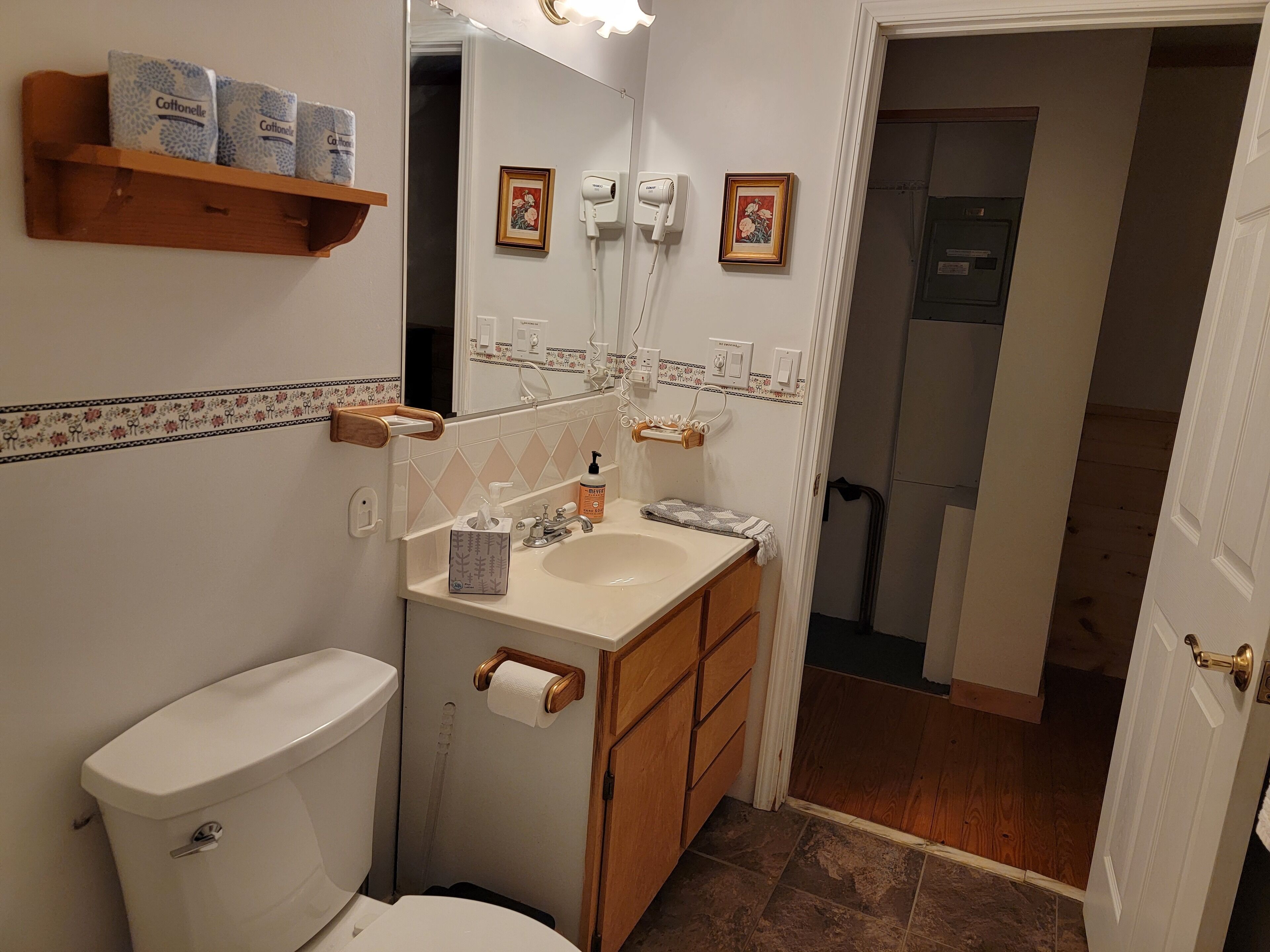 A bathroom with a toilet, sink, and mirror. There are toilet paper and hand soap on the counter.