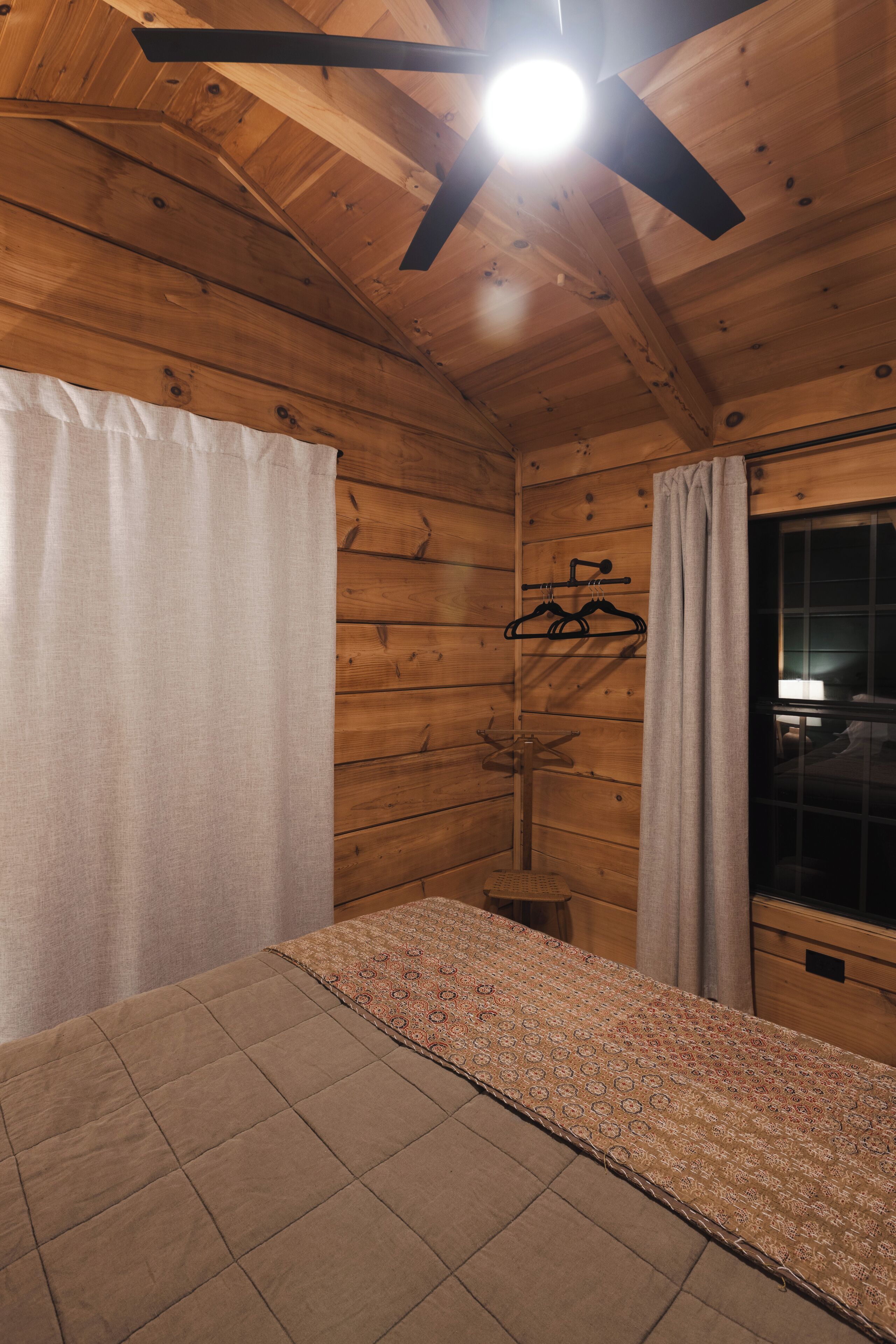 Une pièce en bois avec un lit, une fenêtre et un ventilateur de plafond.