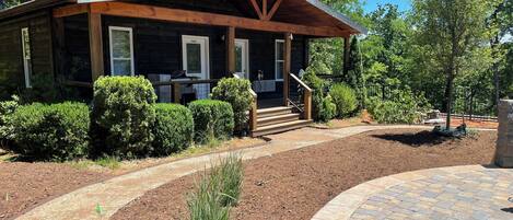 A rustic cabin with a wooden exterior, a porch, and a stone pathway leading to the entrance.