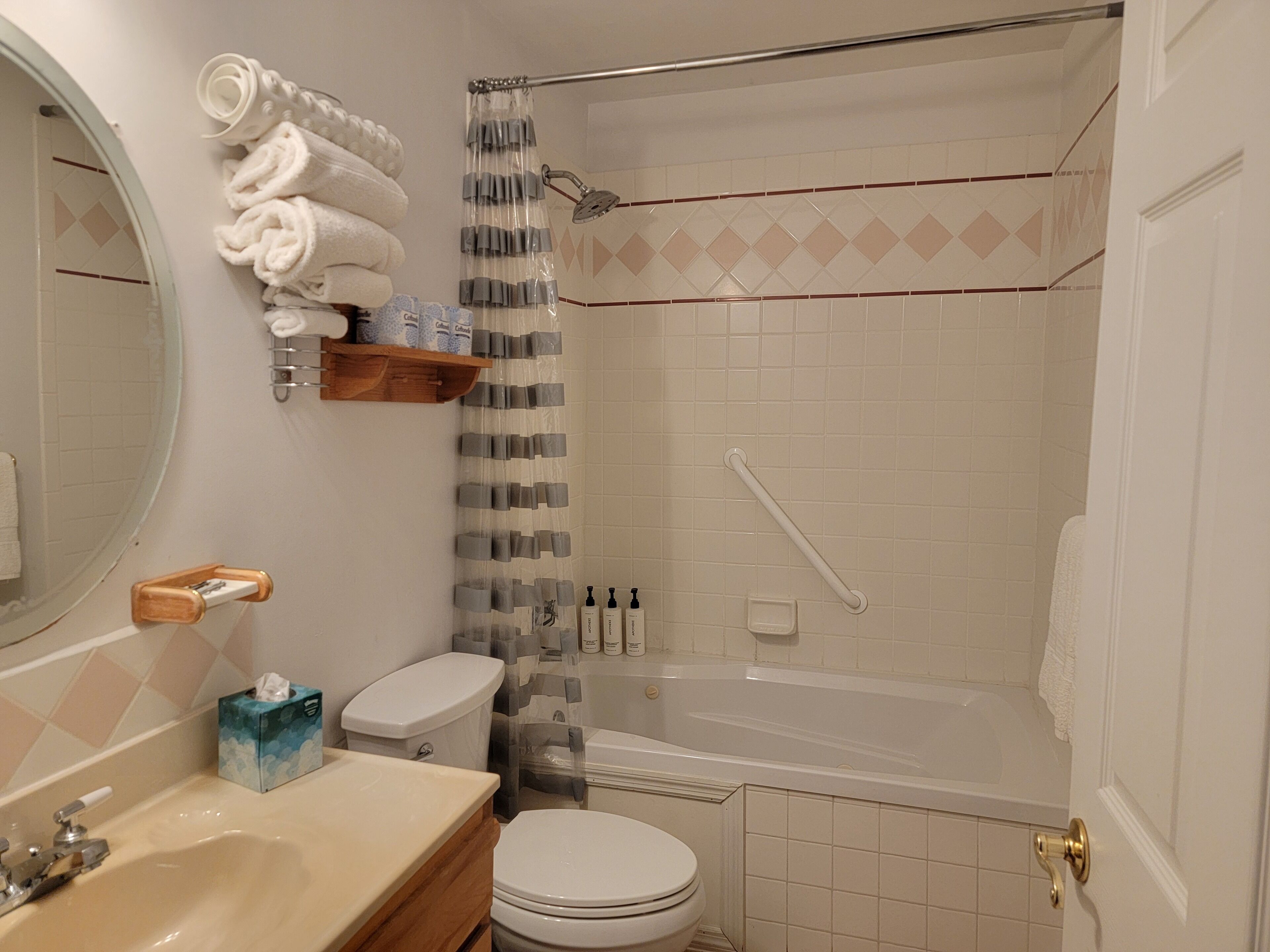 Une salle de bain avec des toilettes, un lavabo et une baignoire. Des serviettes sont pliées et empilées sur une étagère, et il y a un rideau de douche.