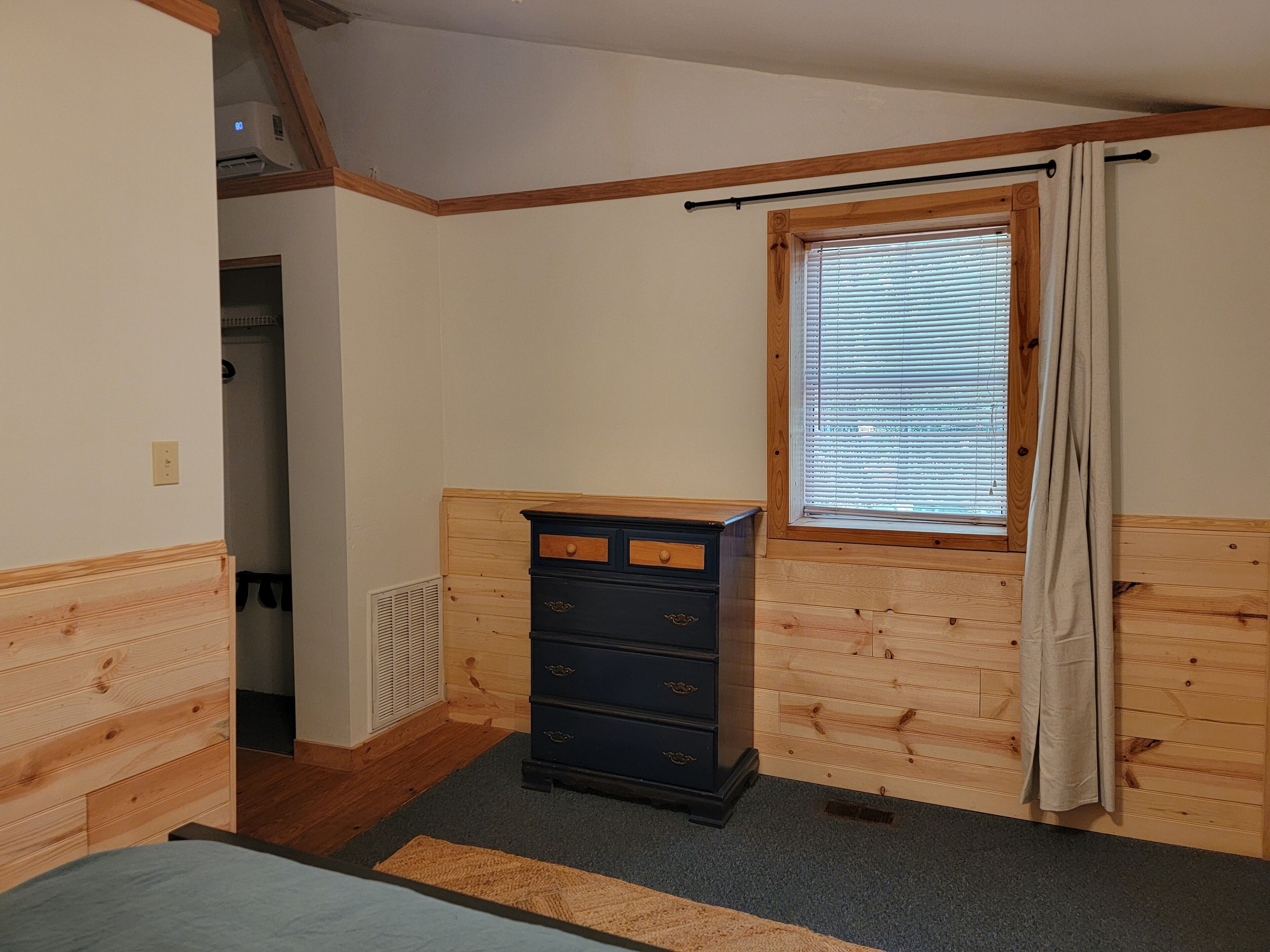 A room with wooden paneling, a window with blinds, a black dresser, and a radiator.