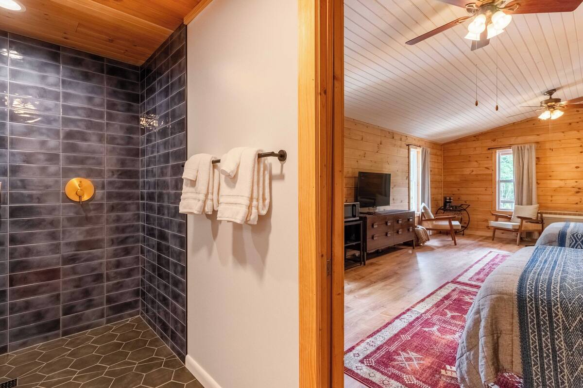 A bathroom with dark tiled walls, a wooden ceiling, and a shower area.
