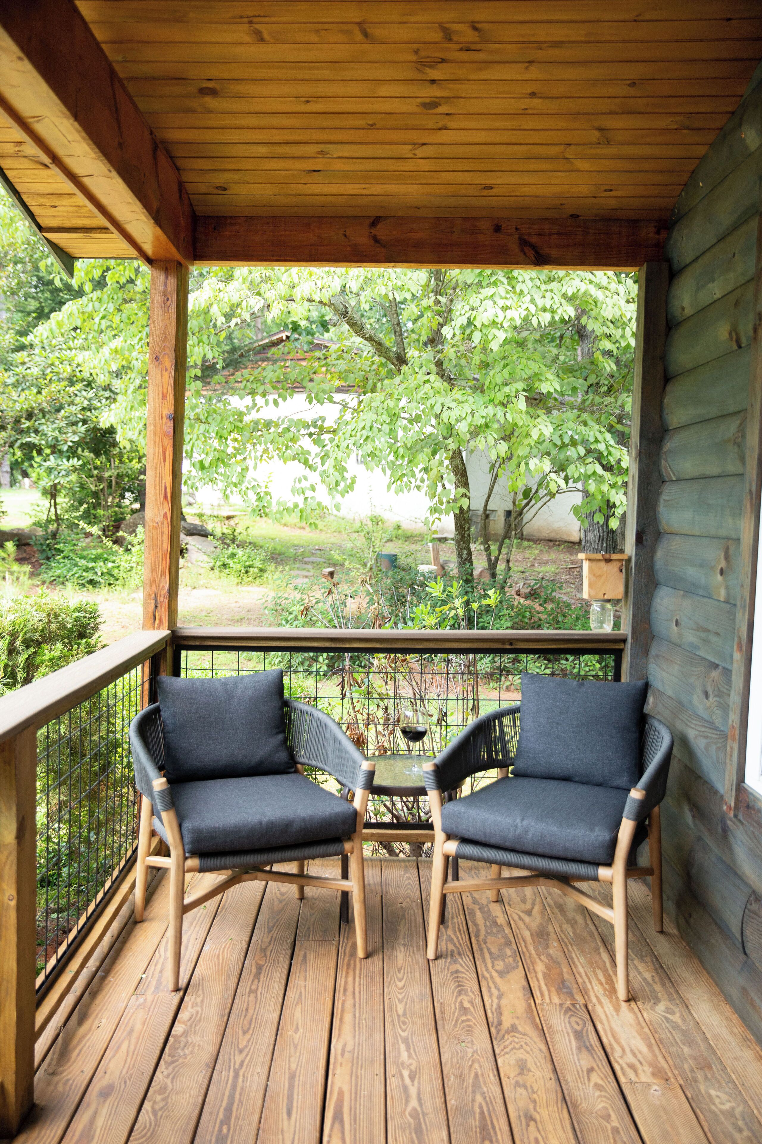 Une terrasse en bois avec deux chaises et une table, donnant sur un jardin agrémenté d’arbres et d’une clôture.