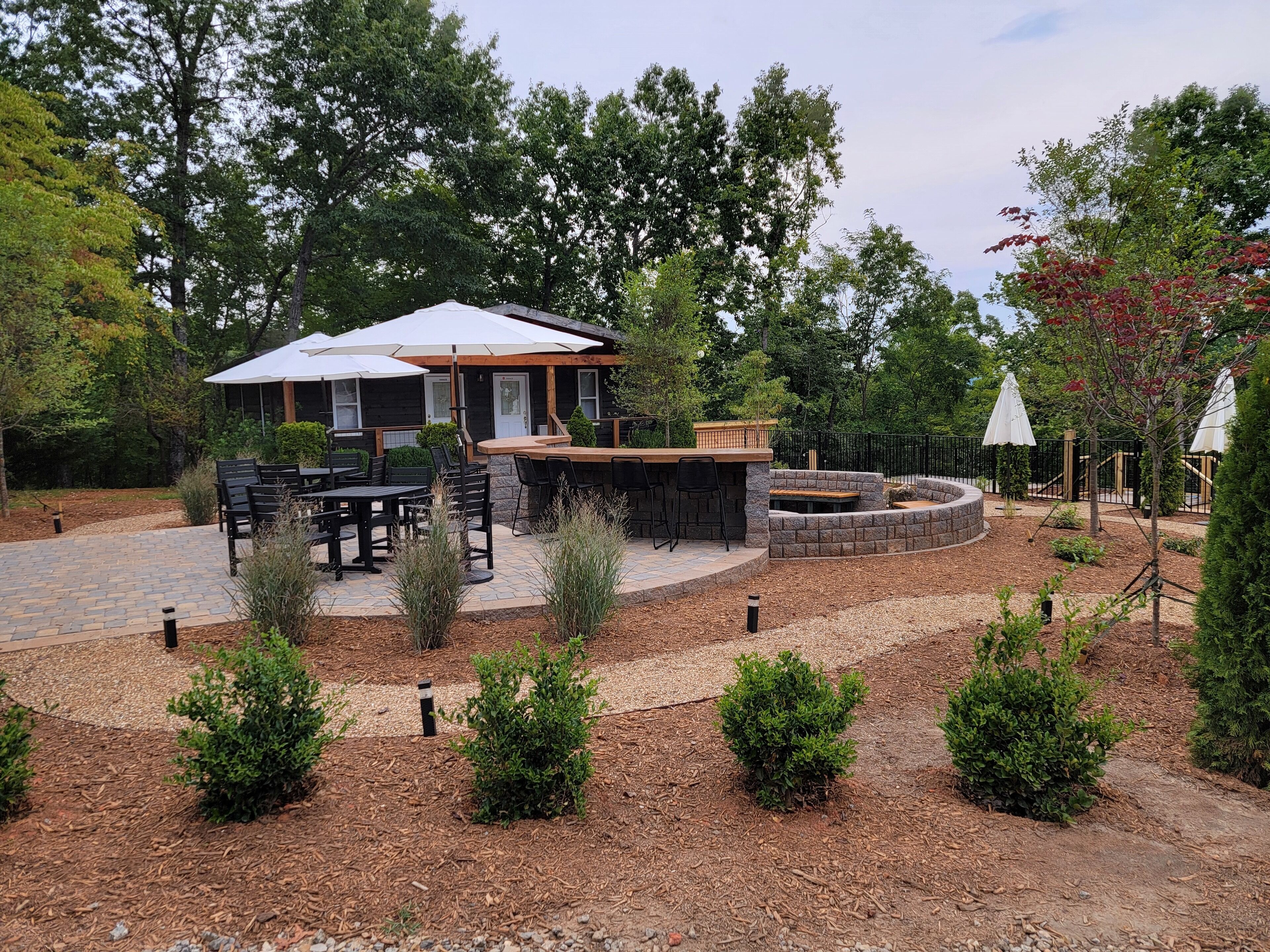An outdoor patio area with a stone fire pit, black metal chairs, and a wooden table.