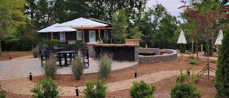 An outdoor patio area with a stone fire pit, black metal chairs, and a wooden table.