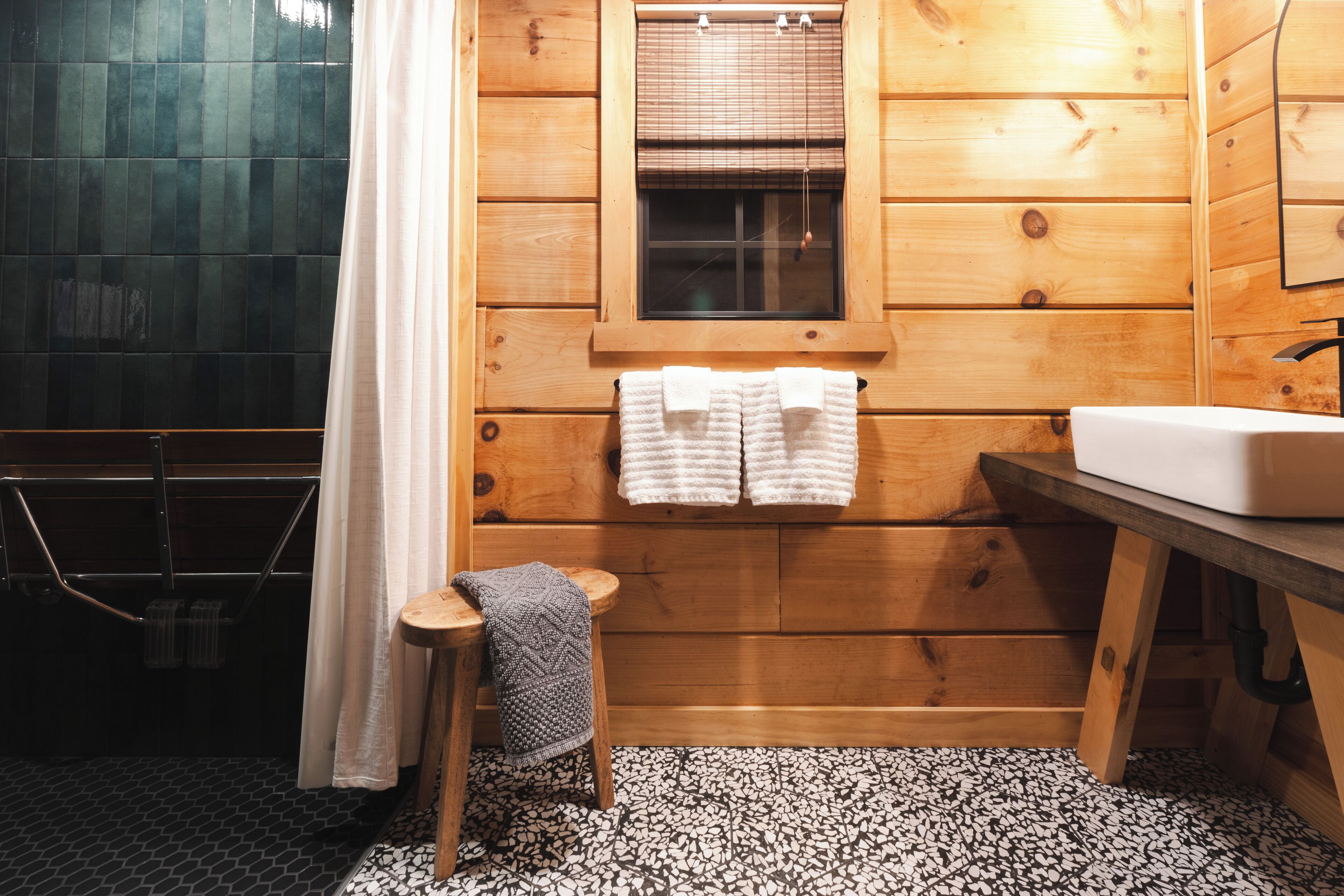 Une salle de bain rustique, aménagée dans une cabane en bois, avec une fenêtre, un lavabo et un petit tabouret.