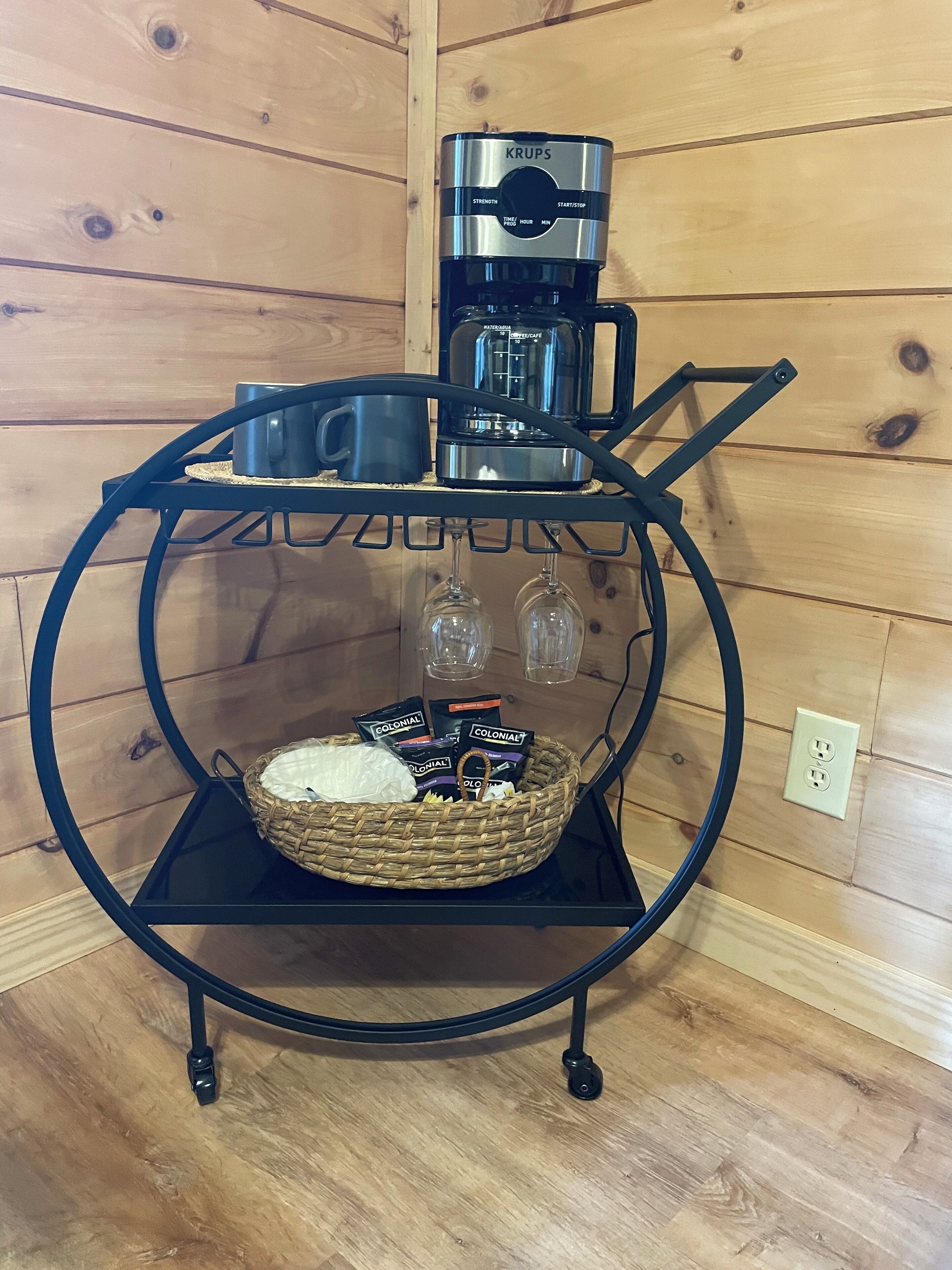 A coffee maker on a black metal stand with a basket containing coffee pods and a white cloth.