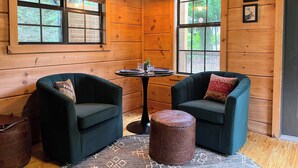 A cozy room with wooden walls, two green armchairs, a small round table, and a brown ottoman. - The Shaded Crest (Adults Only 21+) (Lake Lure)