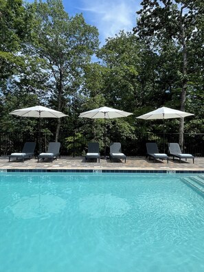 Una piscina al aire libre, sombrillas, sillones reclinables de piscina