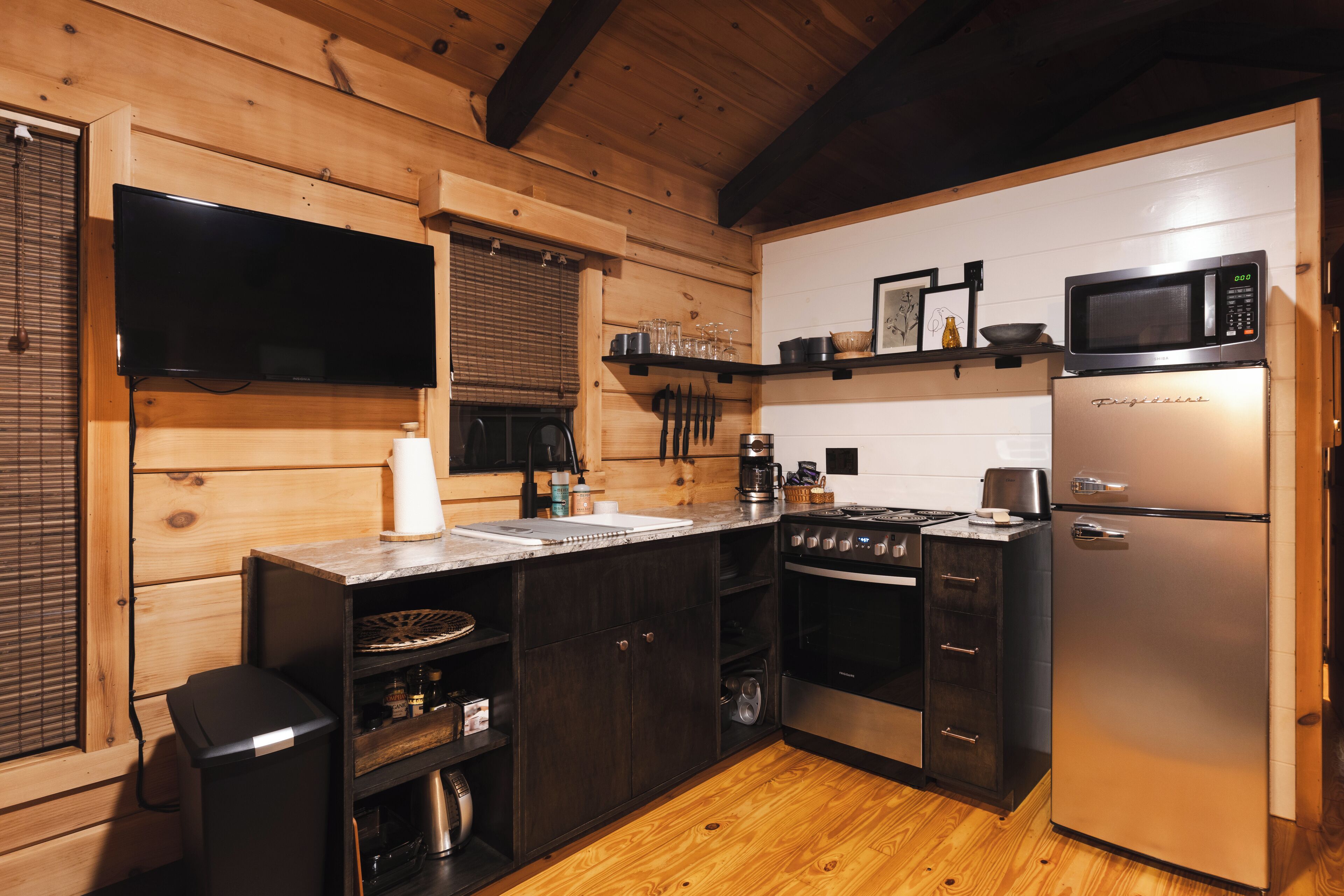 A modern kitchen with wooden walls, a flat-screen TV, a microwave, a refrigerator, and a stove.