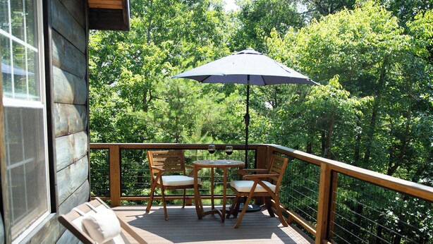 A wooden deck with lounge chairs and a table, surrounded by a wooden railing and trees. - The Shaded Crest (Adults Only 21+) (Lake Lure)