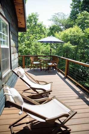 A wooden deck with lounge chairs and a table, surrounded by a wooden railing and trees. - The Shaded Crest (Adults Only 21+) (Lake Lure)