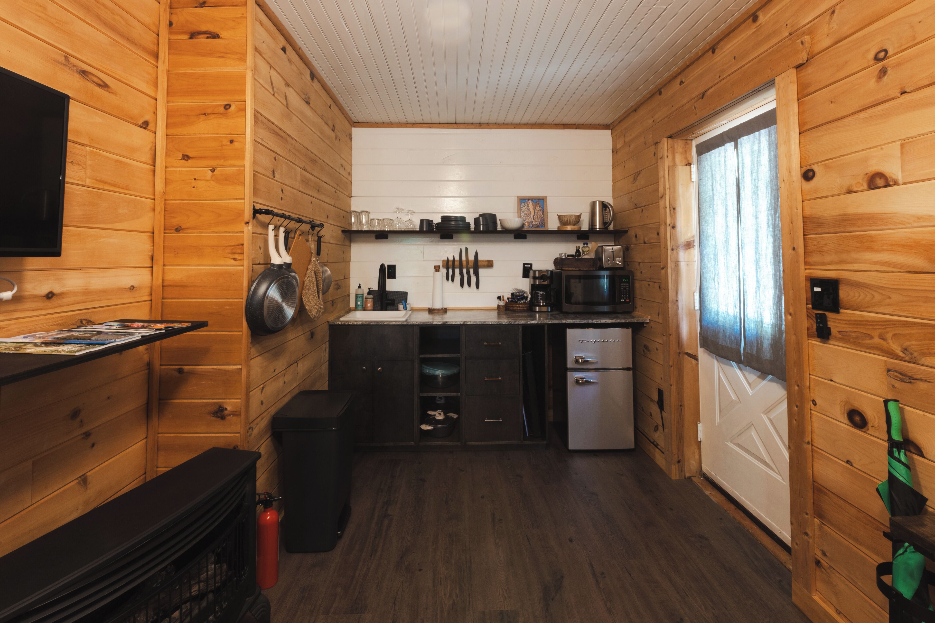 Une cuisine compacte avec des murs en bois, un réfrigérateur, un four à micro-ondes et une machine à café.