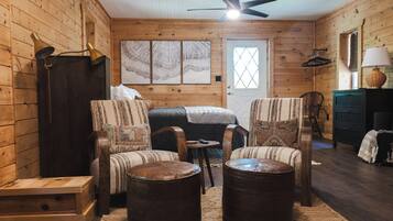 A cozy log cabin room with a bed, two armchairs, a small table, and a ceiling fan.