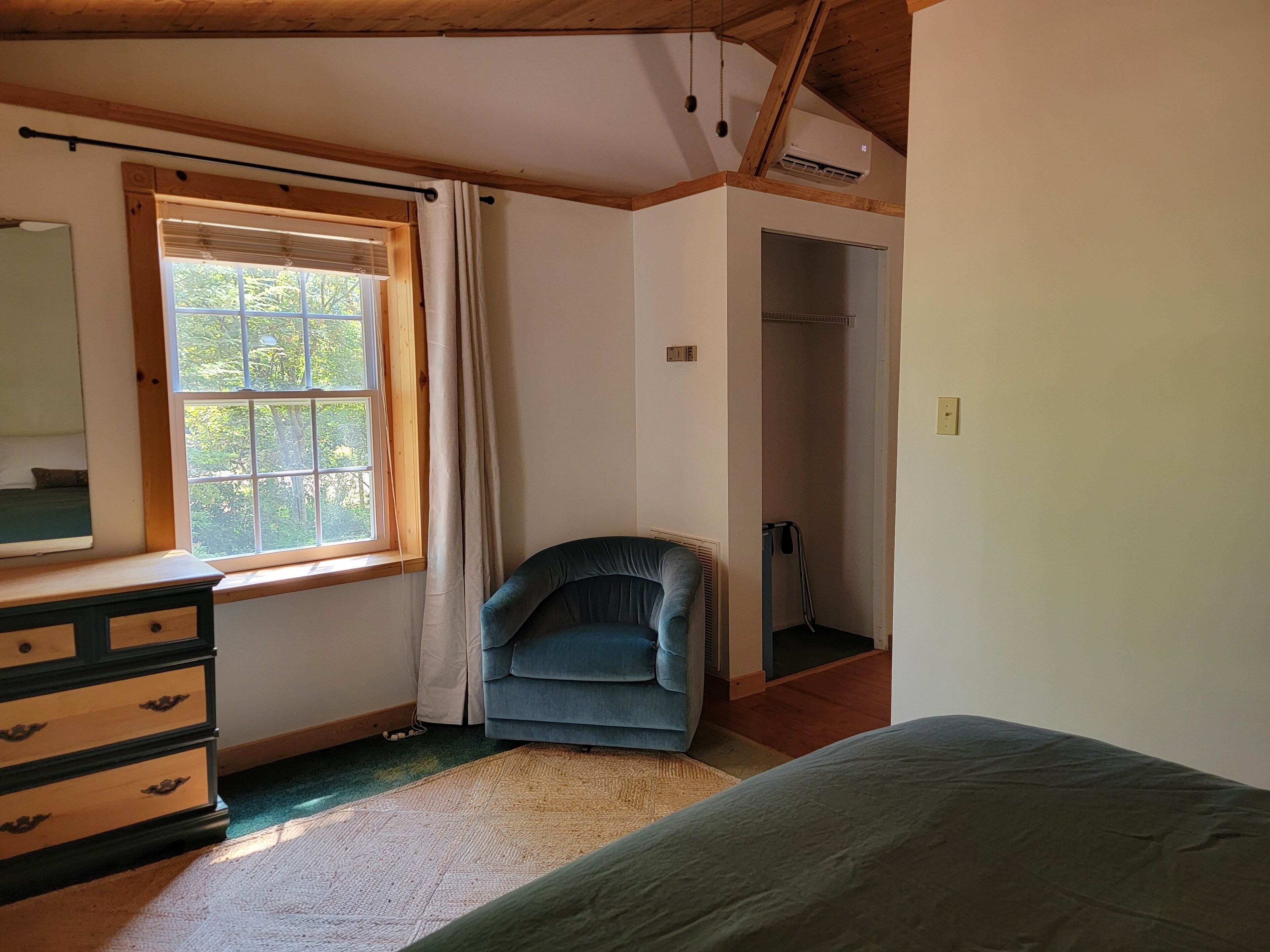 Un dormitorio con cama, cómoda, ventana con cortinas y una silla.