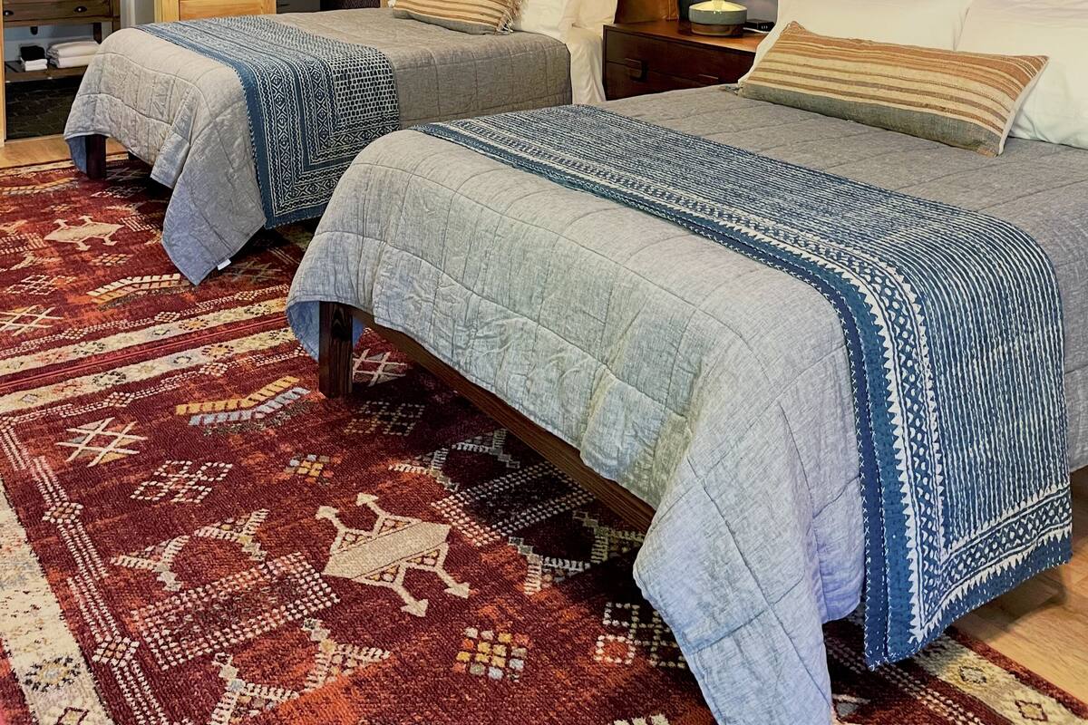 A hotel room with two beds, a wooden wardrobe, a mirror, and a patterned rug.