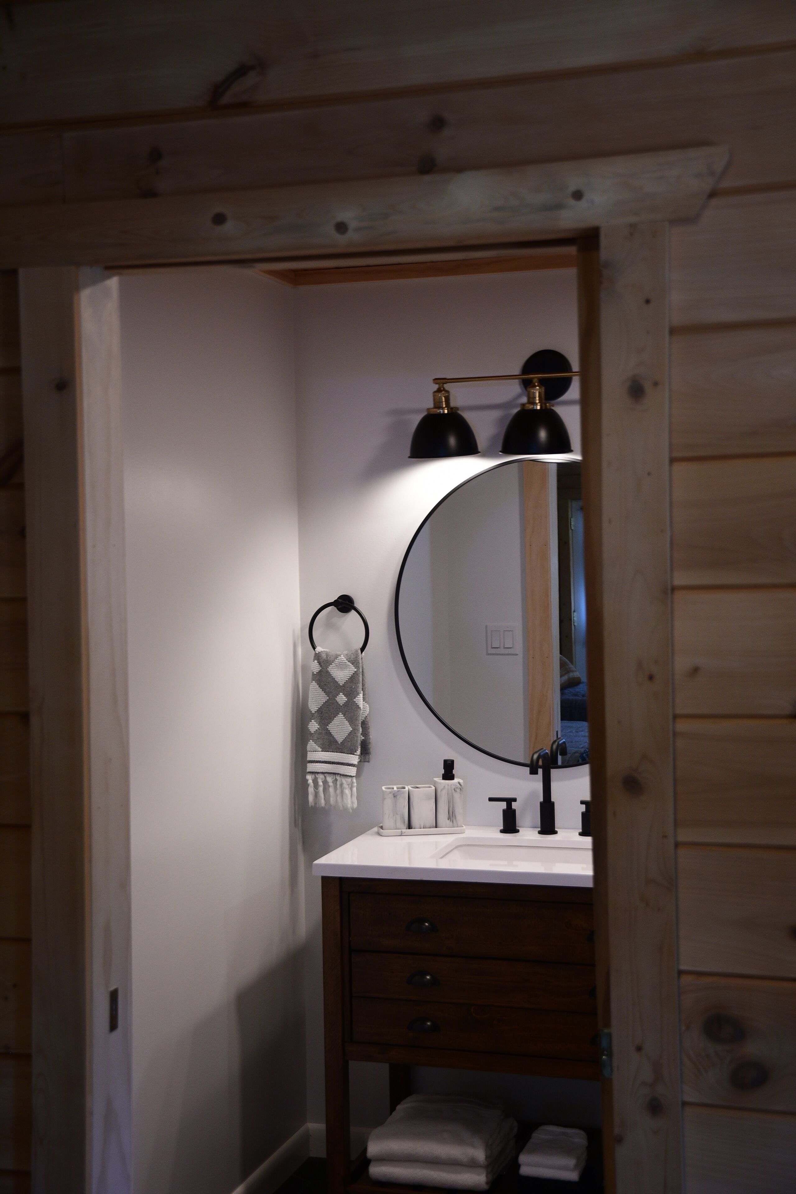 Een badkamer met een houten wastafelmeubel, een ronde spiegel en een handdoekhouder.