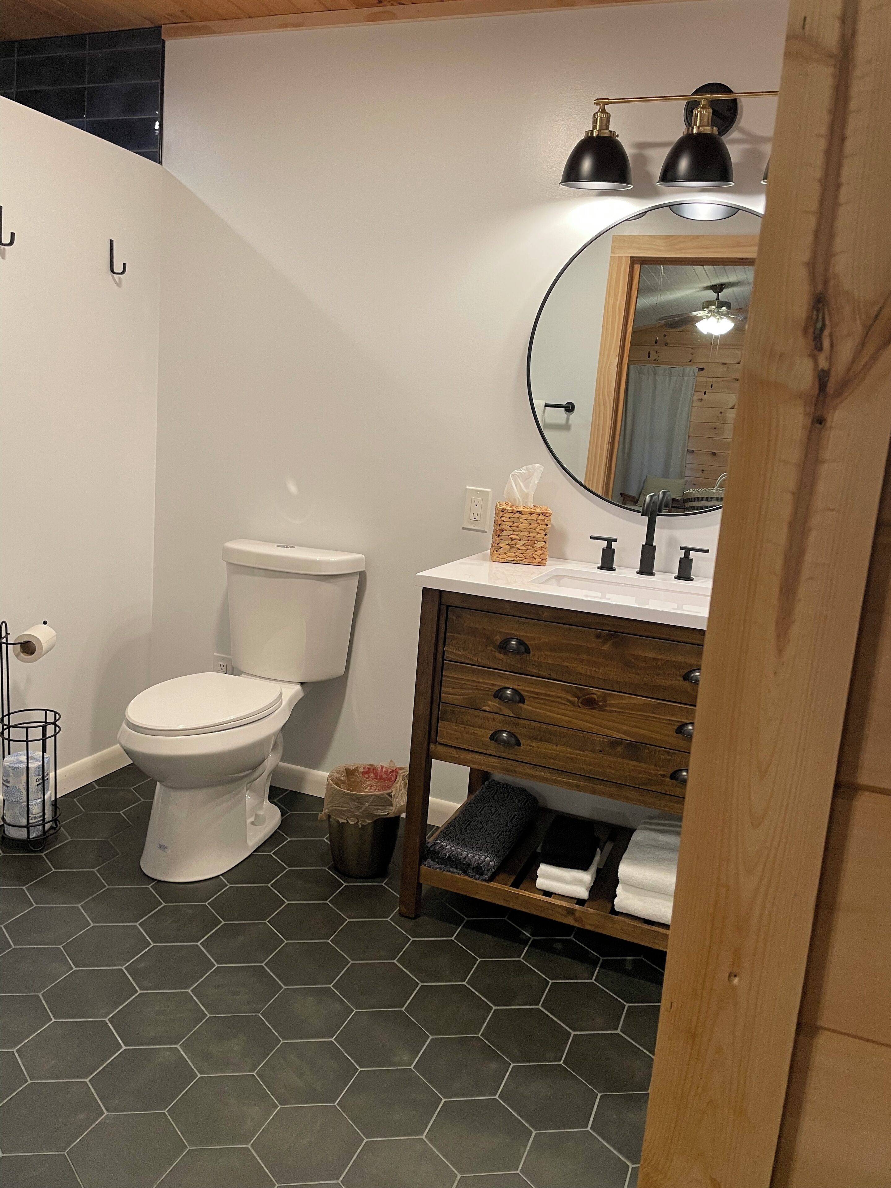 A bathroom with a white toilet, a wooden vanity with a mirror, and a hexagonal tile floor.