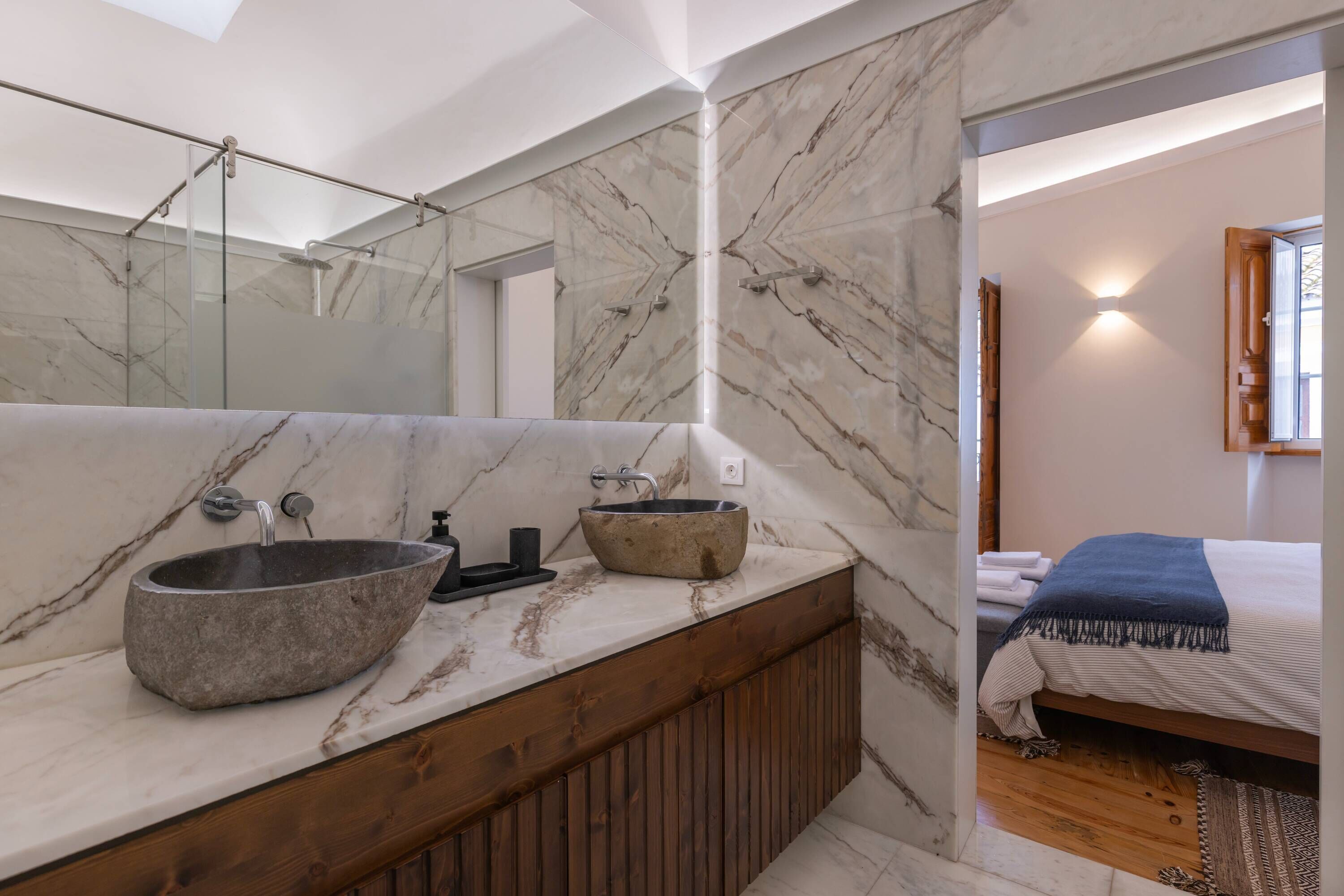 Een moderne badkamer met een marmeren wastafelmeubel, een grote spiegel en een houten bad.