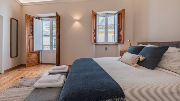 A bedroom with a large bed, wooden door, and a window with open shutters.