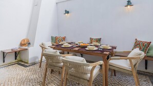 A dining area with a wooden table and wicker chairs, surrounded by white walls and a tiled floor.