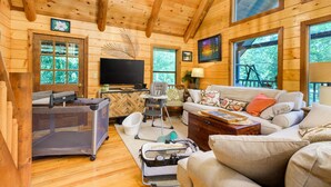 Ein gemütliches Holzblockhaus-Interieur mit Fernseher, Sofa und Spielecke für Babys.