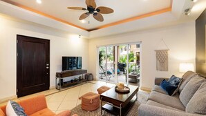A modern living room with a TV, sofa, coffee table, and a ceiling fan. - Tamarindo Beach Condo – 2BR Steps from Sea. (Tamarindo)