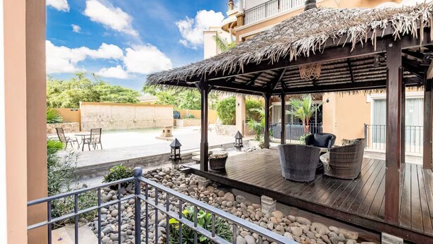 A covered outdoor area with a wooden deck, wicker furniture, and a thatched roof structure. - Tamarindo Beach Condo – 2BR Steps from Sea. (Tamarindo)