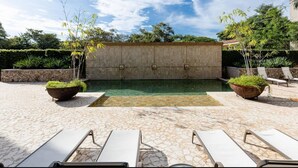 A pool area with stone flooring, two large planters, and white lounge chairs. - Tamarindo Beach Condo – 2BR Steps from Sea. (Tamarindo)