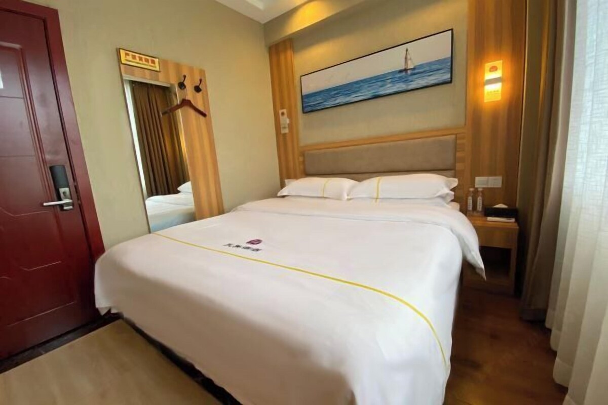 Habitación de hotel con cama, un cuadro, cabecera de madera, mesita de noche y una puerta.
