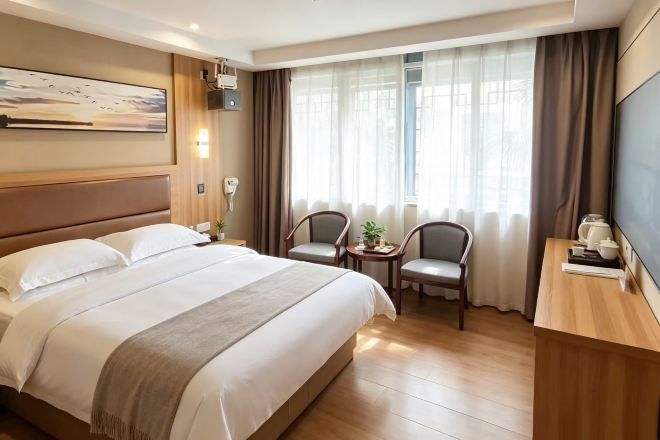 A hotel room with a large bed, two chairs, a small table, a TV, and a window with curtains.