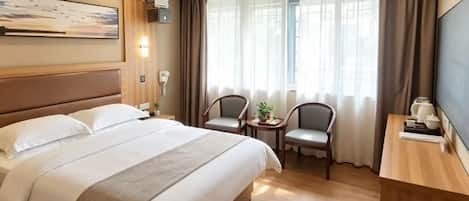 A hotel room with a large bed, two chairs, a small table, a TV, and a window with curtains.