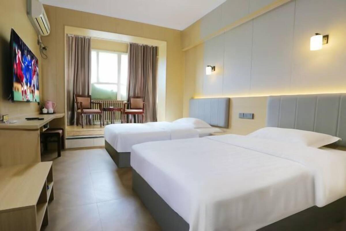 A hotel room with two beds, a desk, a chair, a TV, and a view of the outdoors.