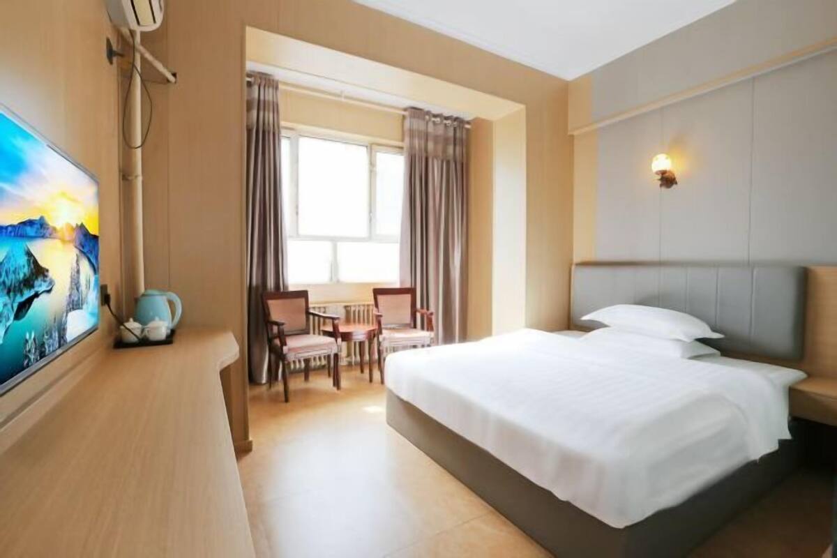 A hotel room with a bed, a desk, a chair, a television, and a window with curtains.