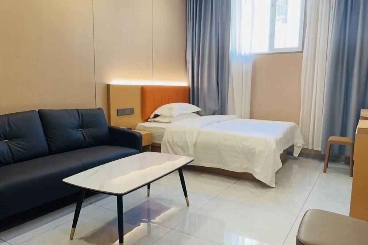 A hotel room with a bed, a sofa, a small table, a nightstand, and a window with curtains.