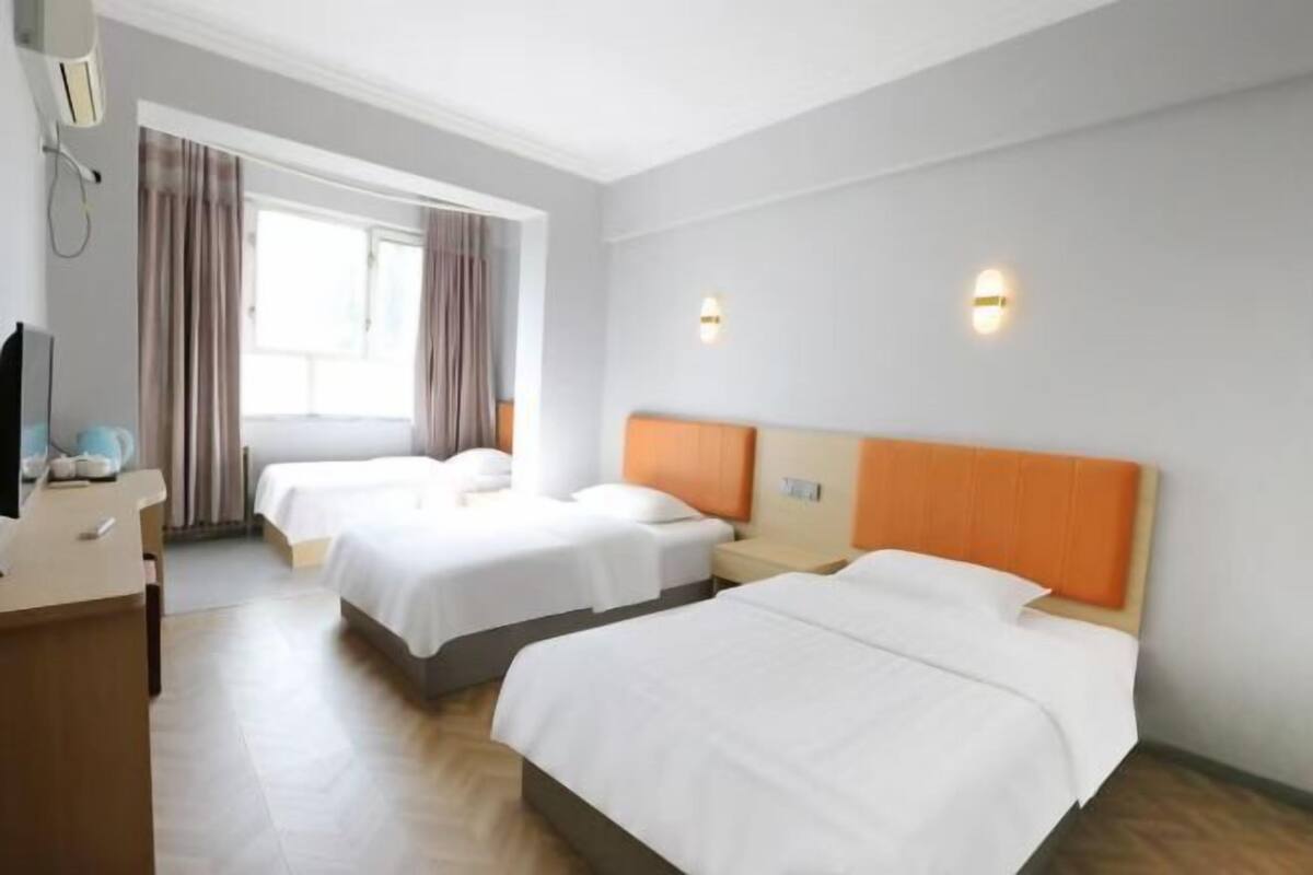 A hotel room with two beds, a desk, a chair, a TV, and a window with curtains.