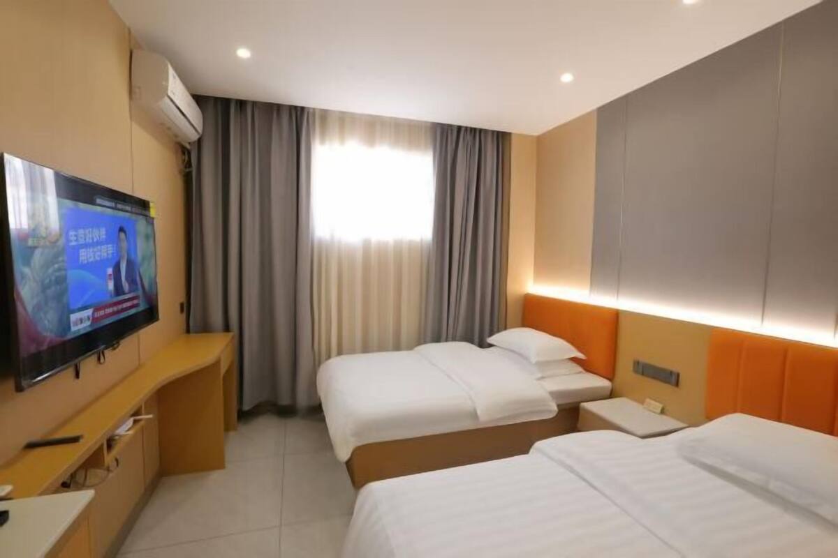 A hotel room with two beds, a TV on a stand, a desk, and a window with curtains.