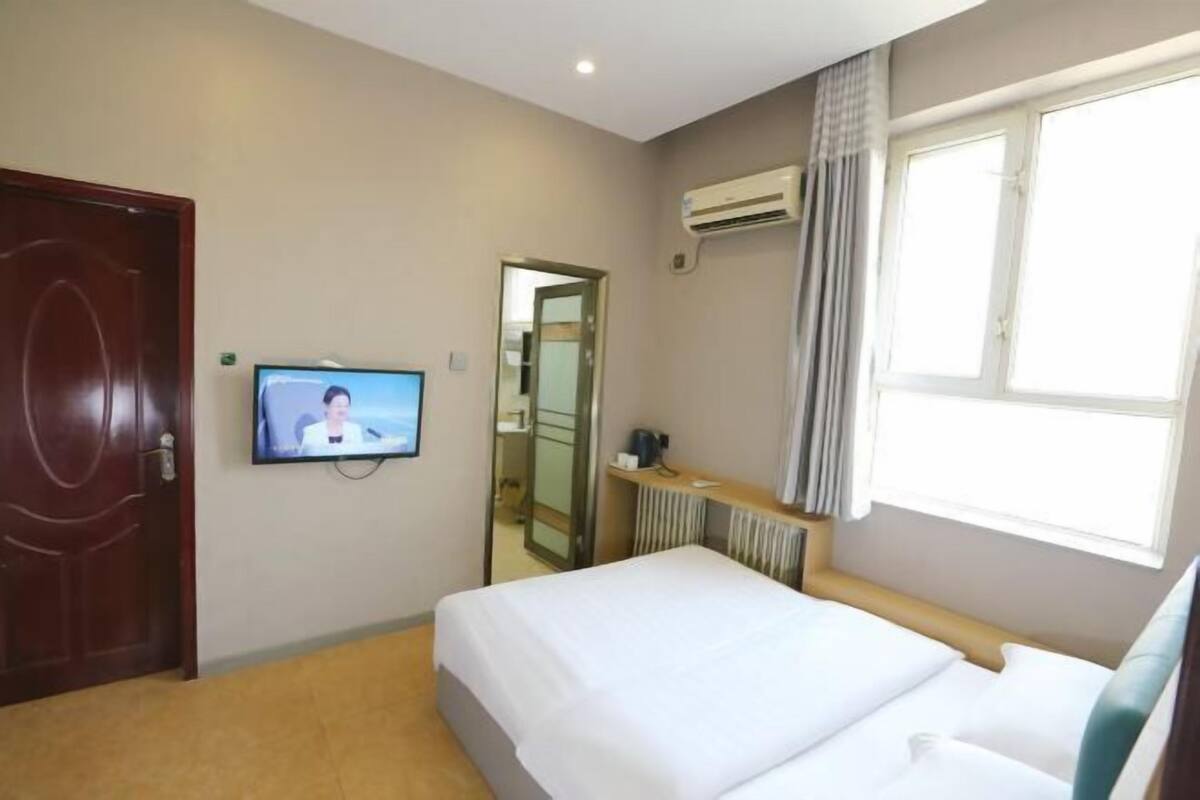 A hotel room with a bed, a television, a window with curtains, and a door.