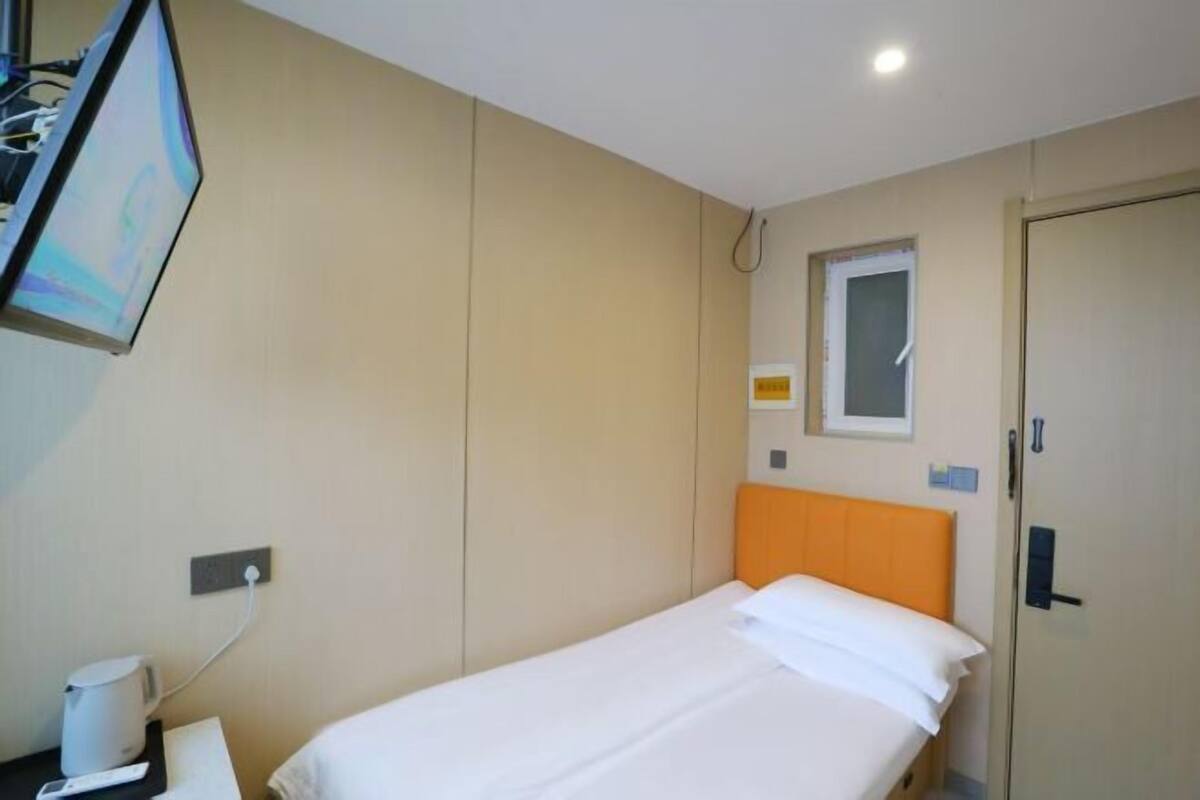 A hotel room with a single bed, a television mounted on the wall, a small window, and a door.