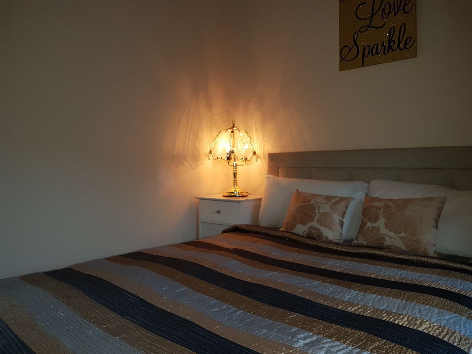 Una camera da letto con un letto, un comodino, una lampada e un cartello appeso al muro.