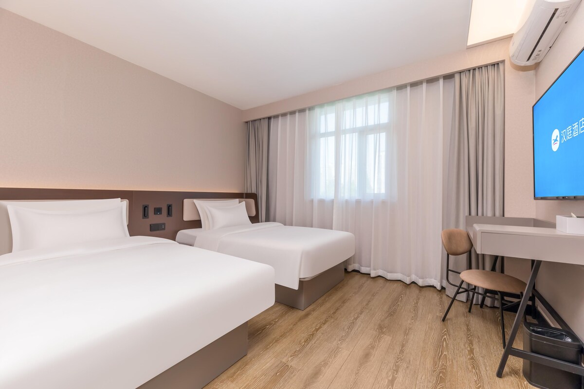 A hotel room with two beds, a desk, a chair, and a TV.
