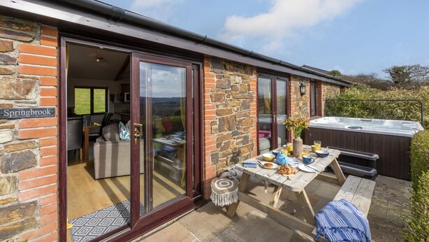 A stone building with a glass door entrance, a hot tub, and a picnic table with outdoor seating. - *3 Bed Bungalow*Near Portreath Beach*Hot Tub*Free Parking & WiFi* (Redruth)