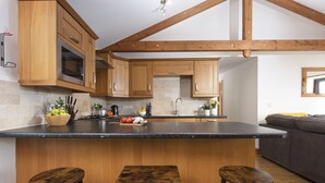 A kitchen with wooden cabinets, a black countertop, and a built-in oven. There are three stools and a sink. - *3 Bed Bungalow*Near Portreath Beach*Hot Tub*Free Parking & WiFi* (Redruth)