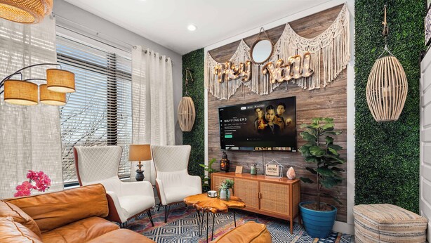 A modern living room with a leather sofa, white armchairs, a TV mounted on a wooden wall, and a patterned rug.